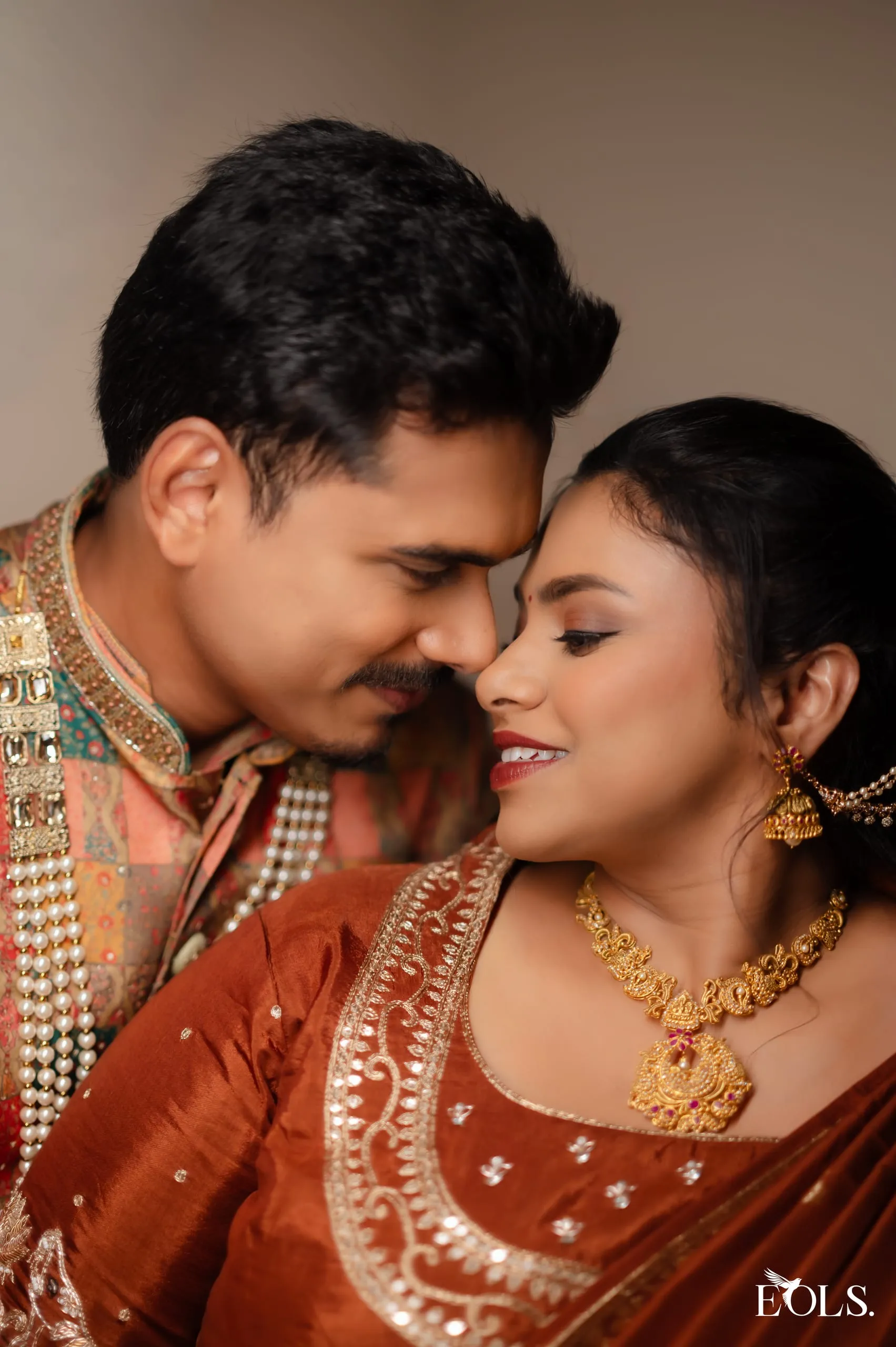 A couple rest their foreheads together, smiling, in engagement attire.