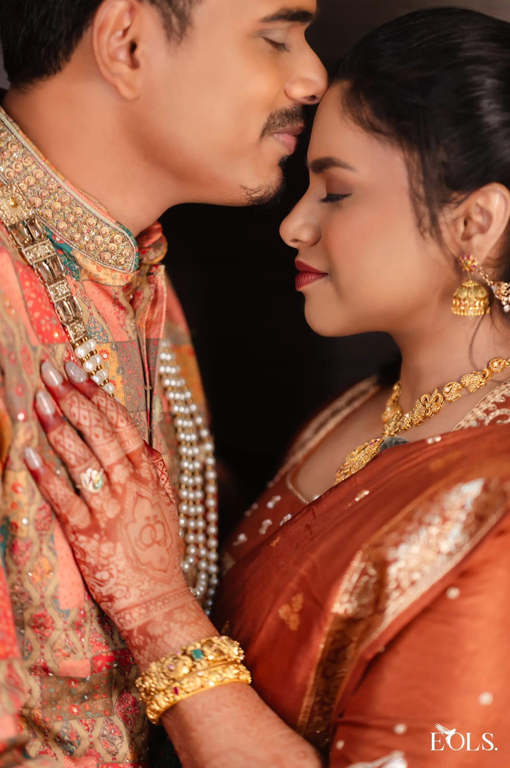 A woman’s hennaed hand rests on a man’s chest, foreheads close.