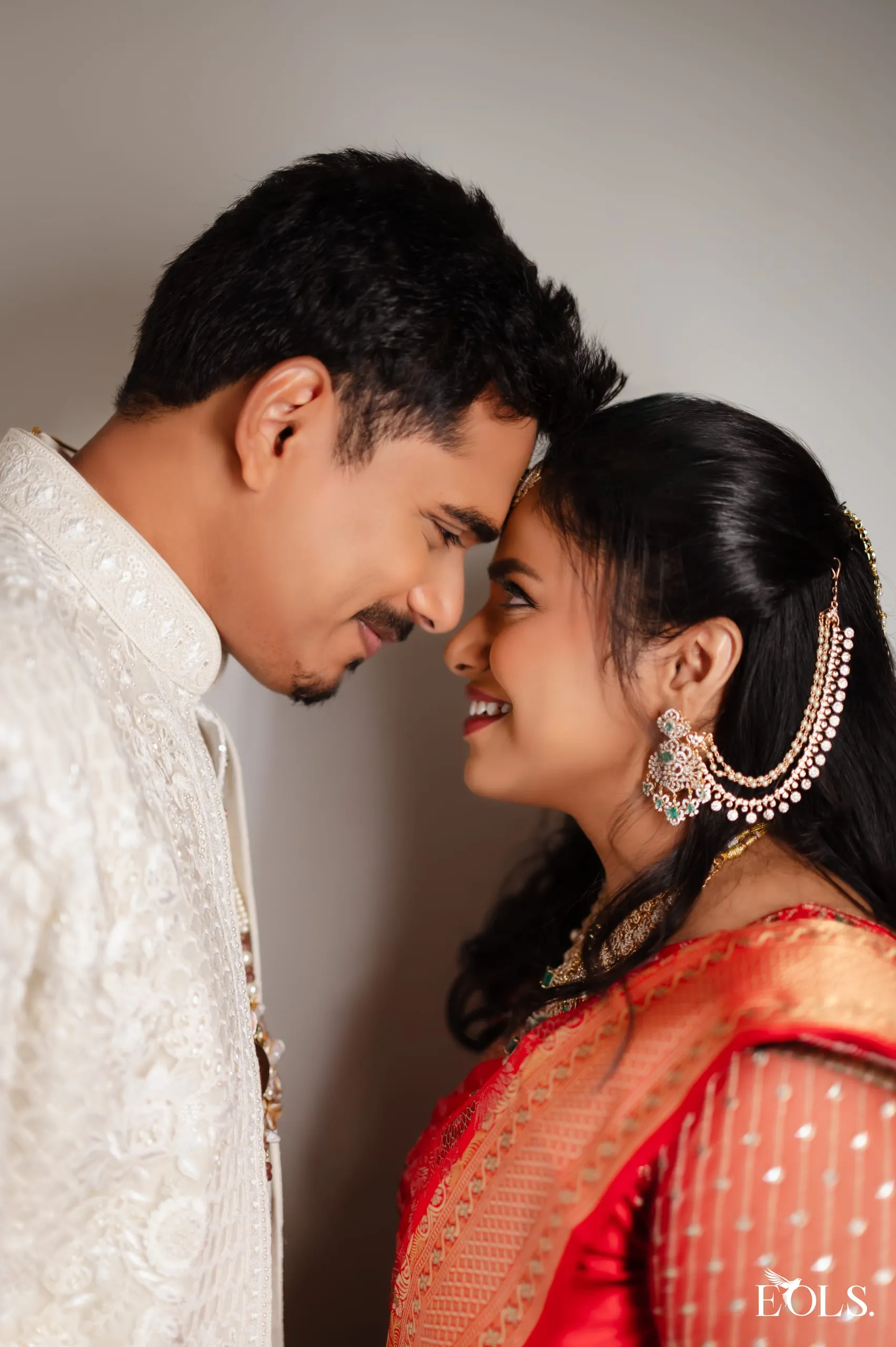 Profile of a couple touching foreheads, he in white, she in red.