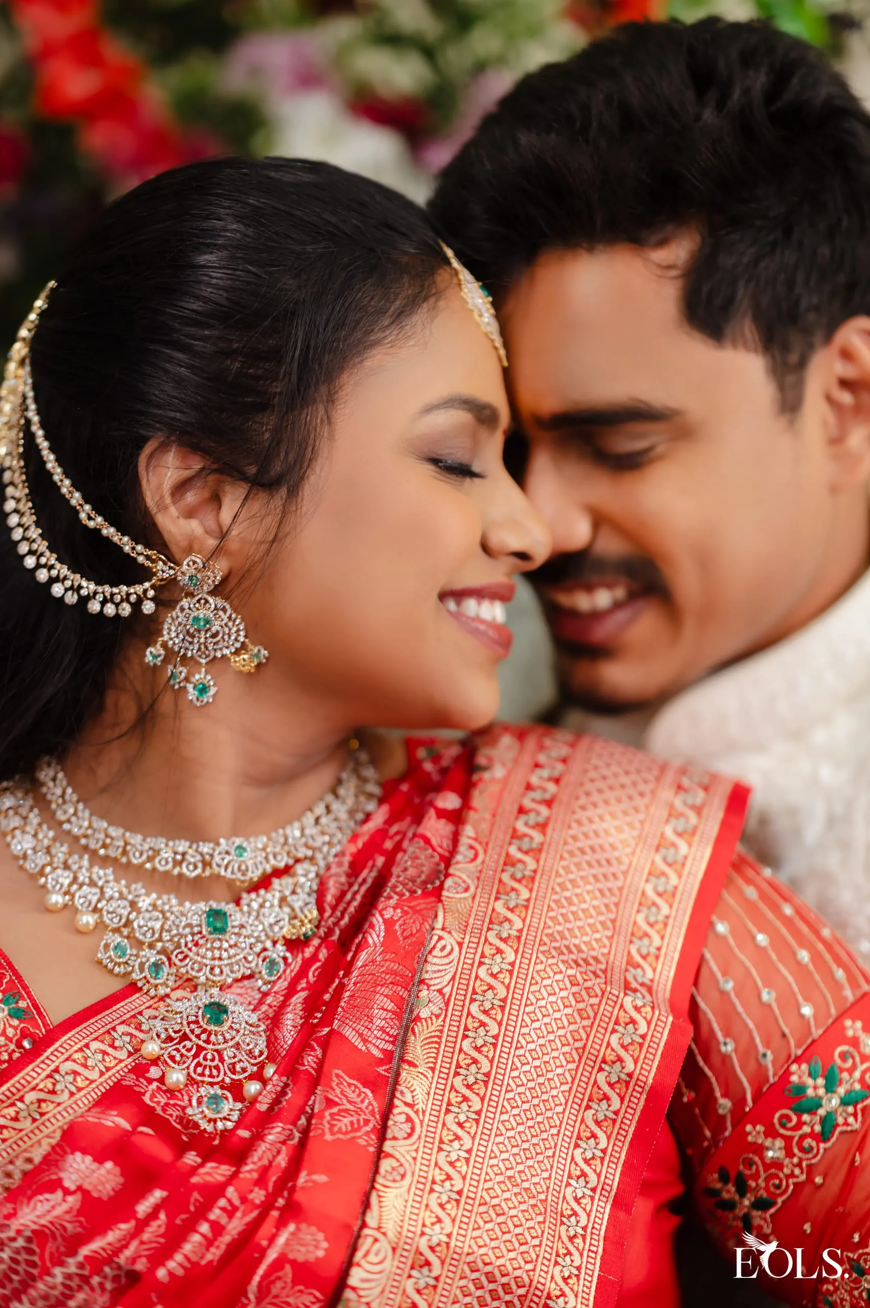 A man nuzzles a laughing woman in a red saree and diamonds.