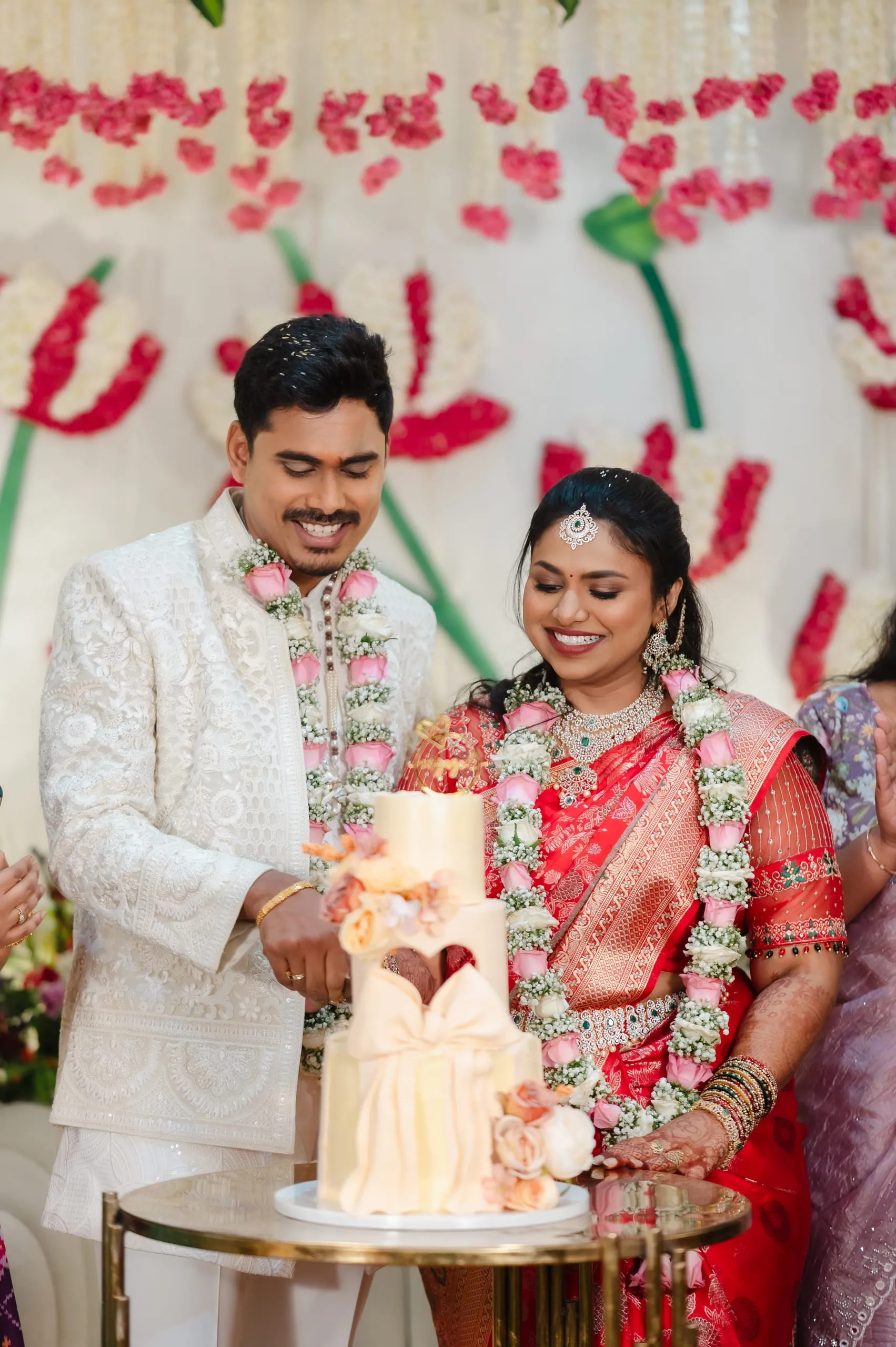 A garlanded couple cut a tiered cake together.