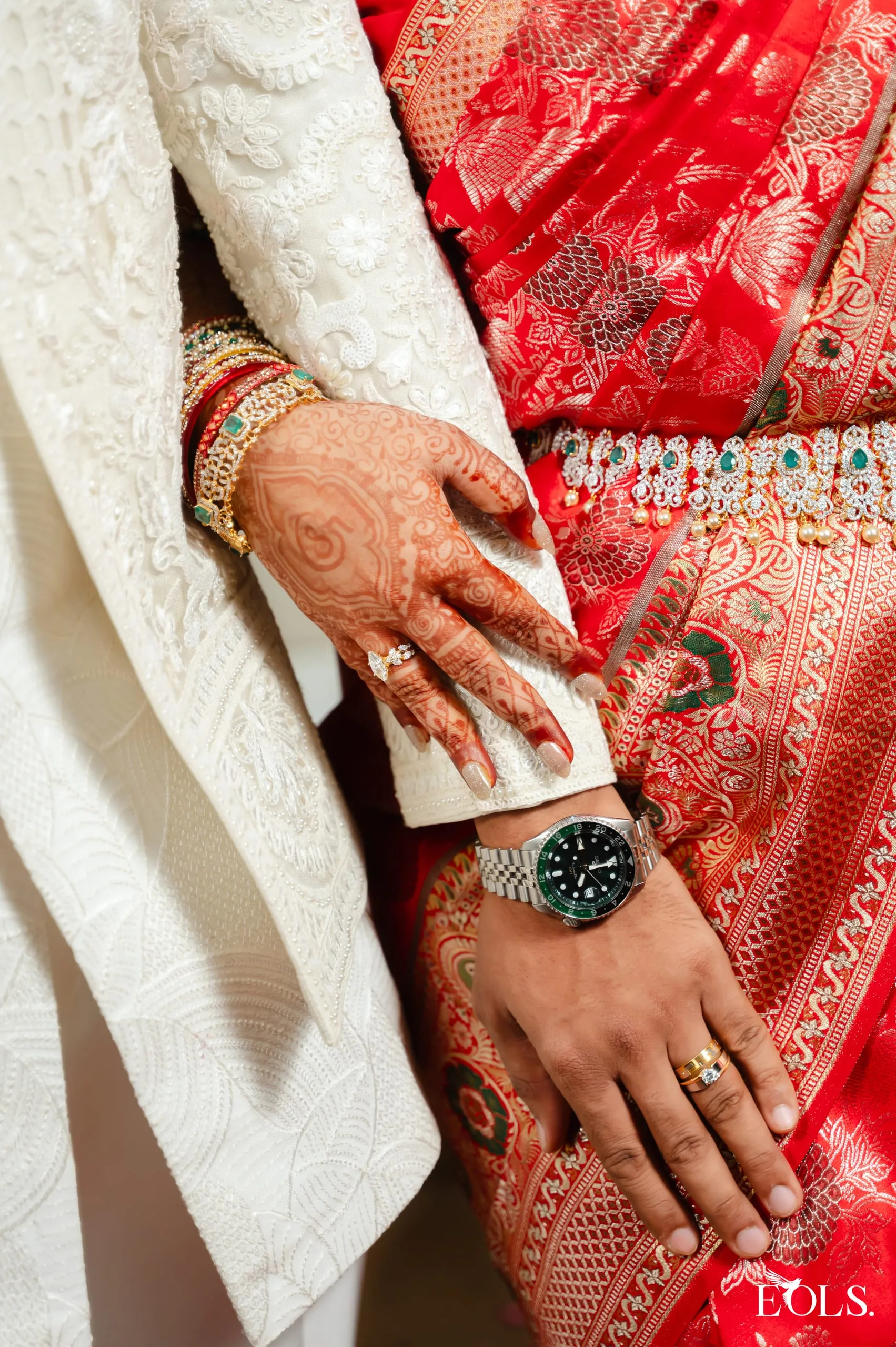 A hennaed hand with a ring rests over a man’s ringed hand.