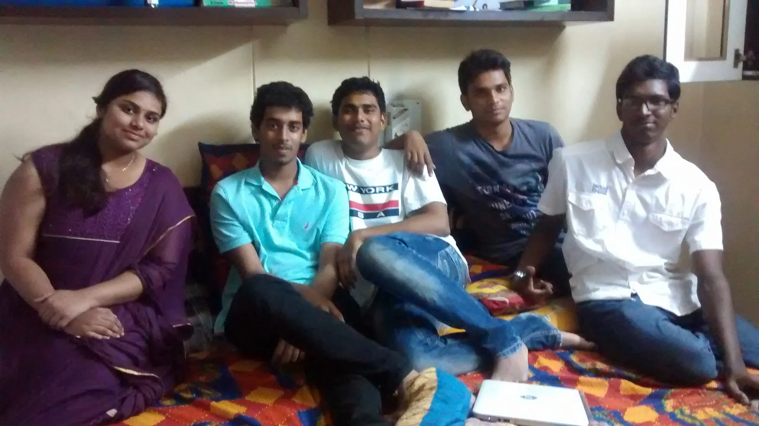Five young friends sit together indoors.