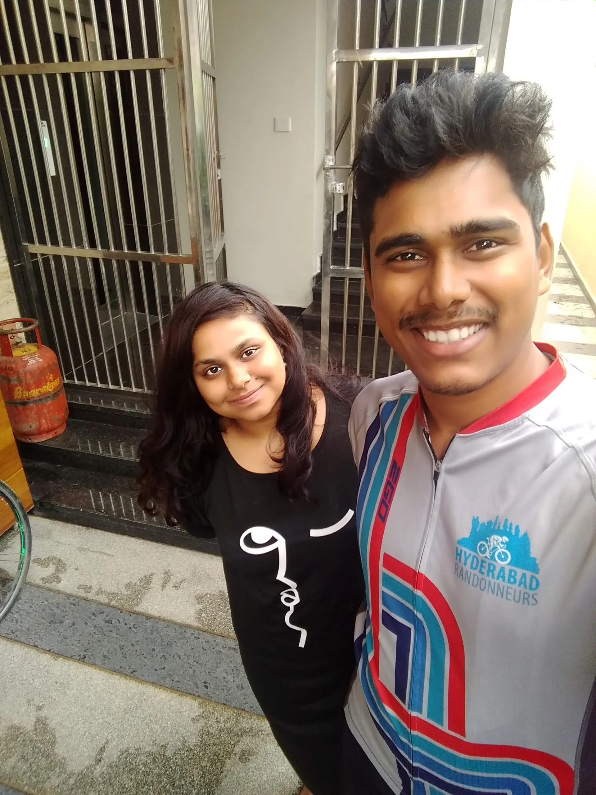 Two friends by a doorway, one in a cycling jersey.