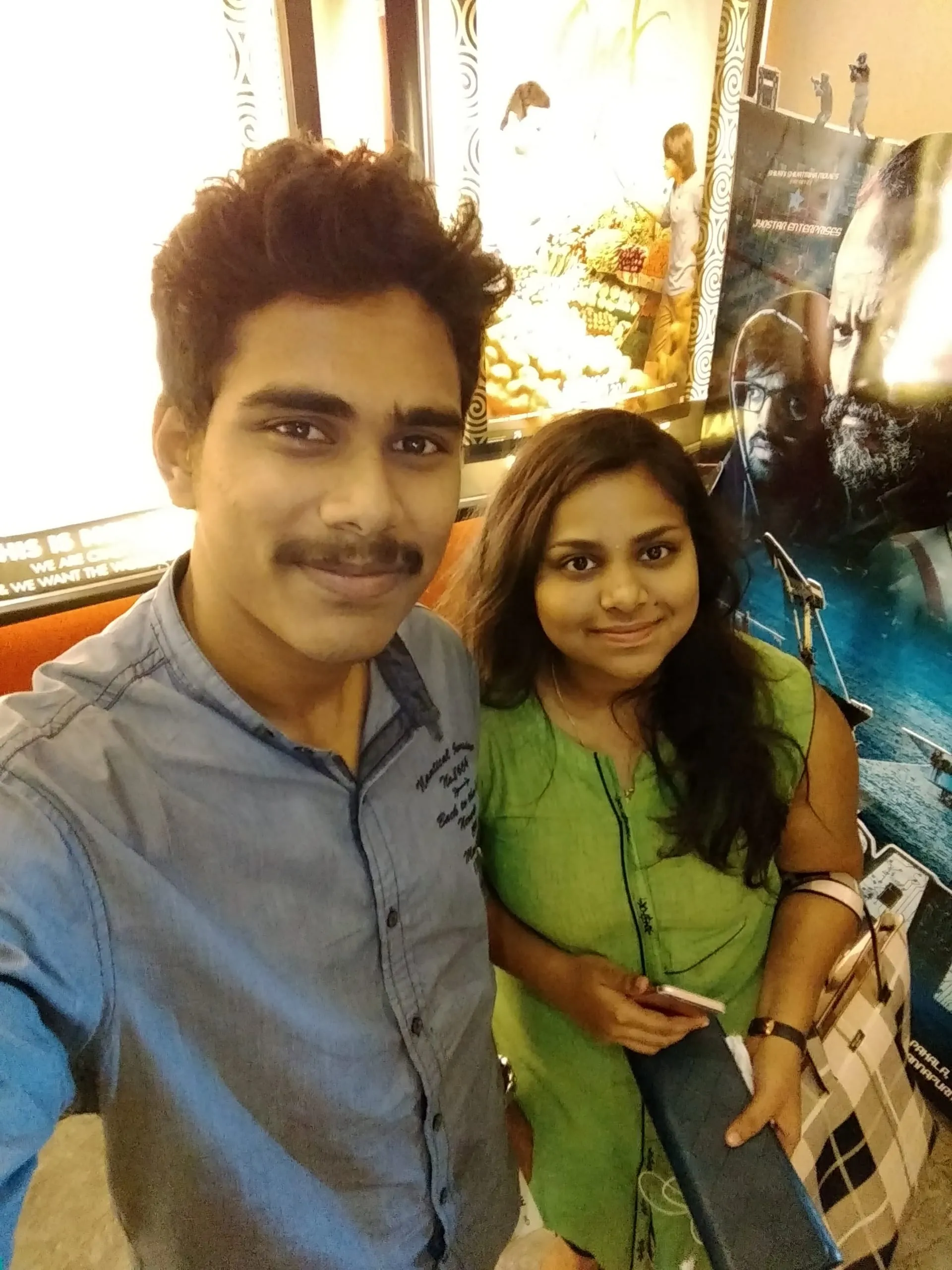 Two friends smile together in a cinema lobby.