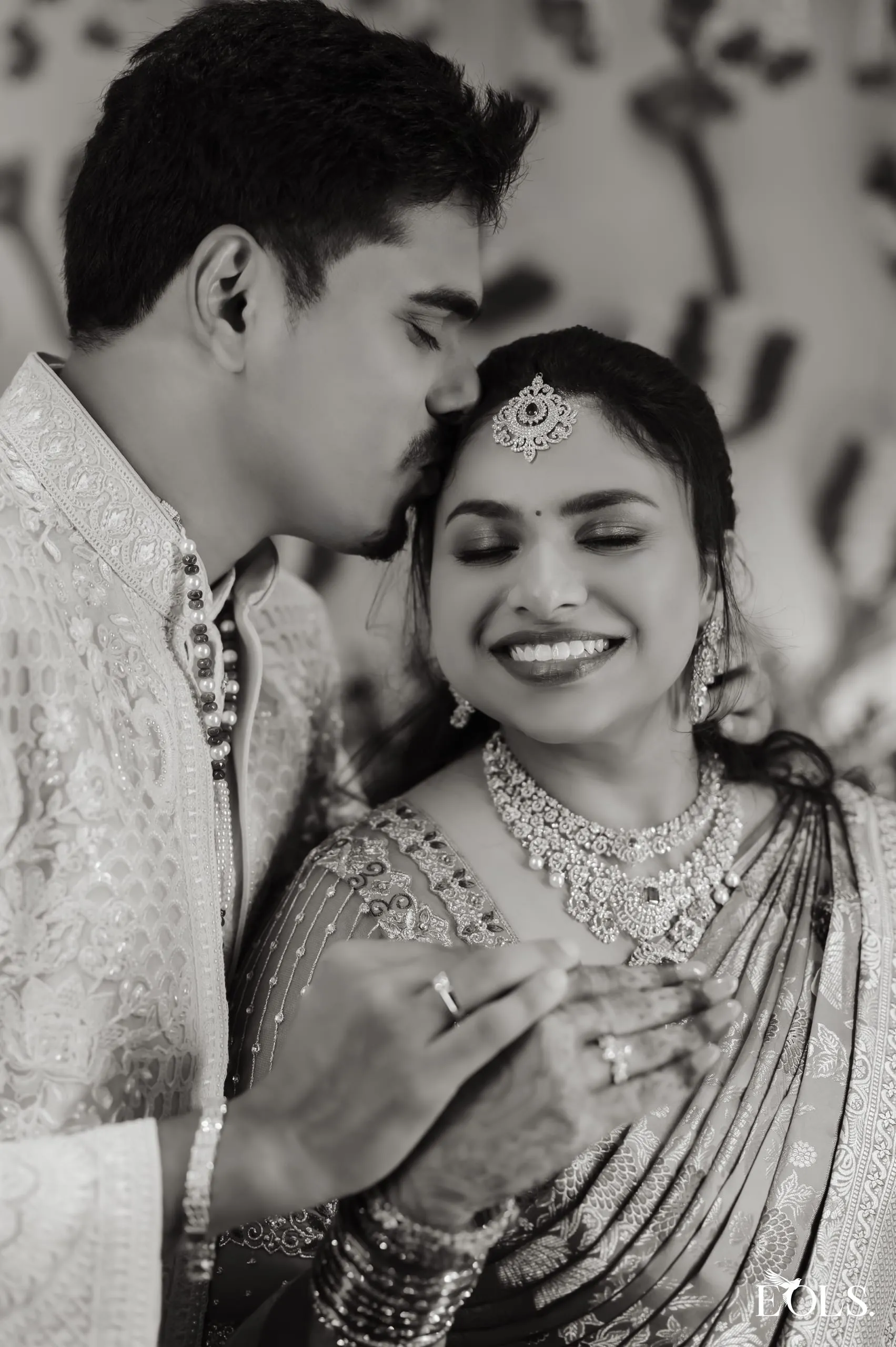 Black and white portrait of Gautham kissing Swathi as she smiles