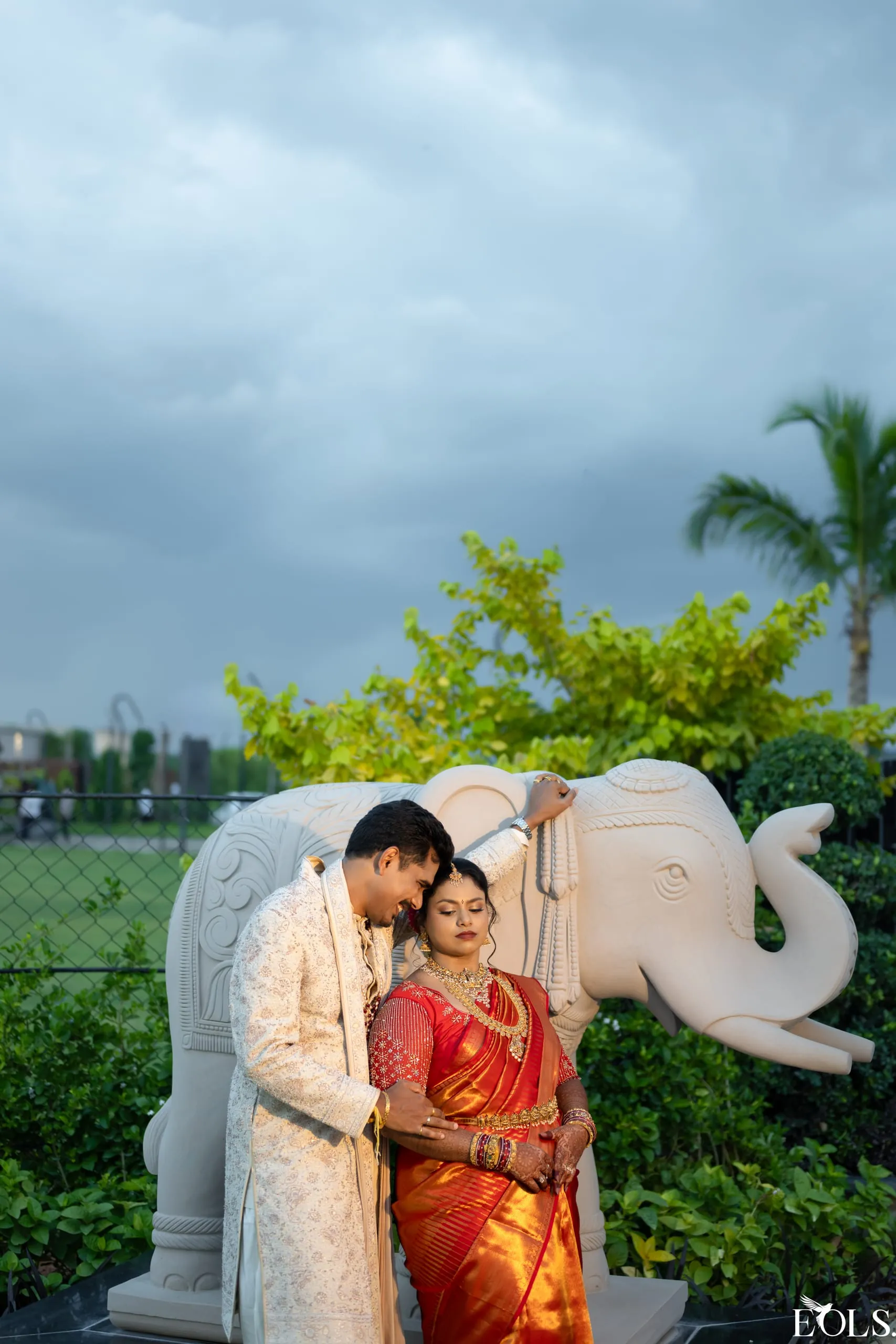 A couple beside a white stone elephant under a dramatic sky.