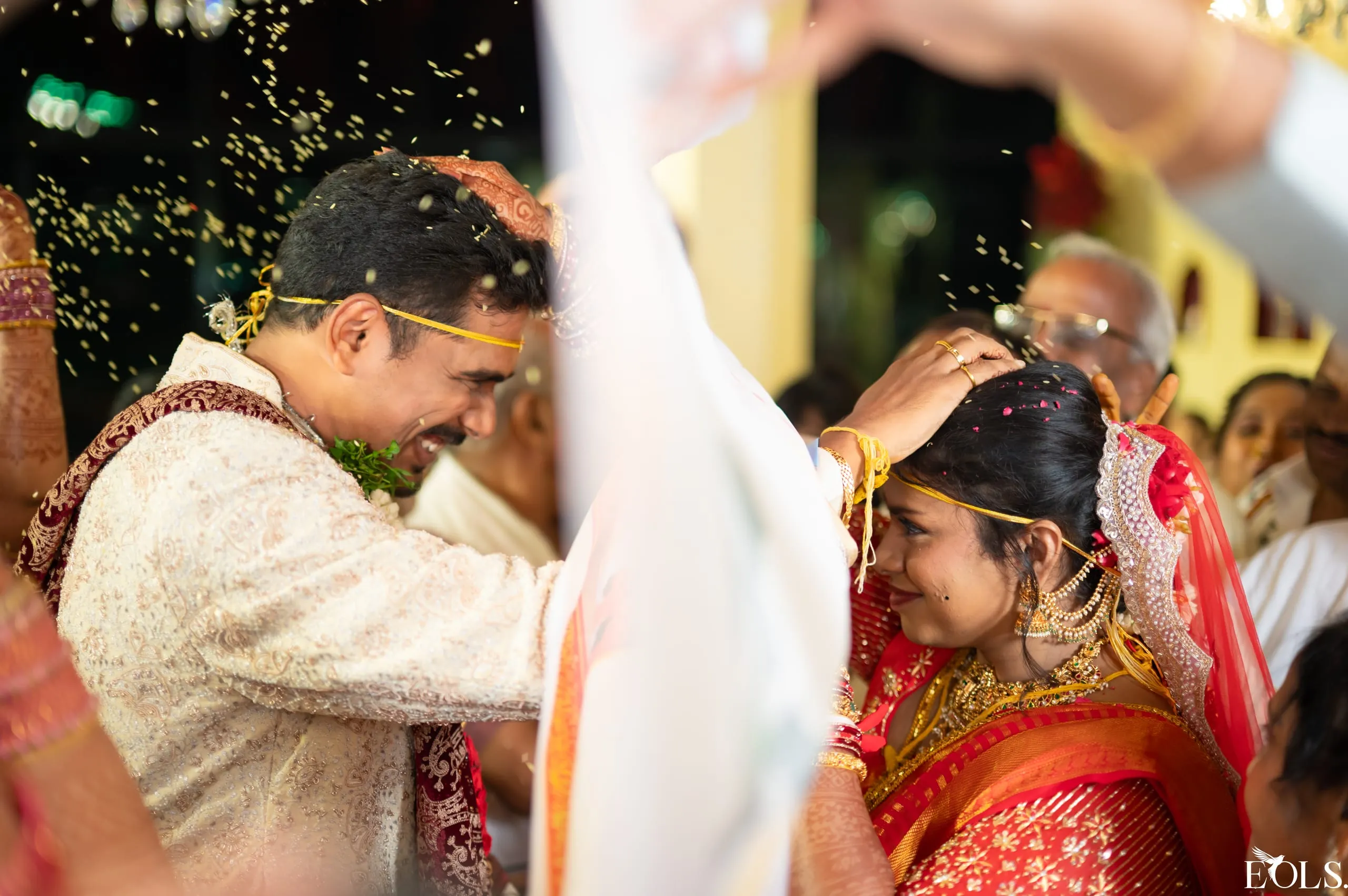 A couple laugh as rice is showered during a wedding ritual.