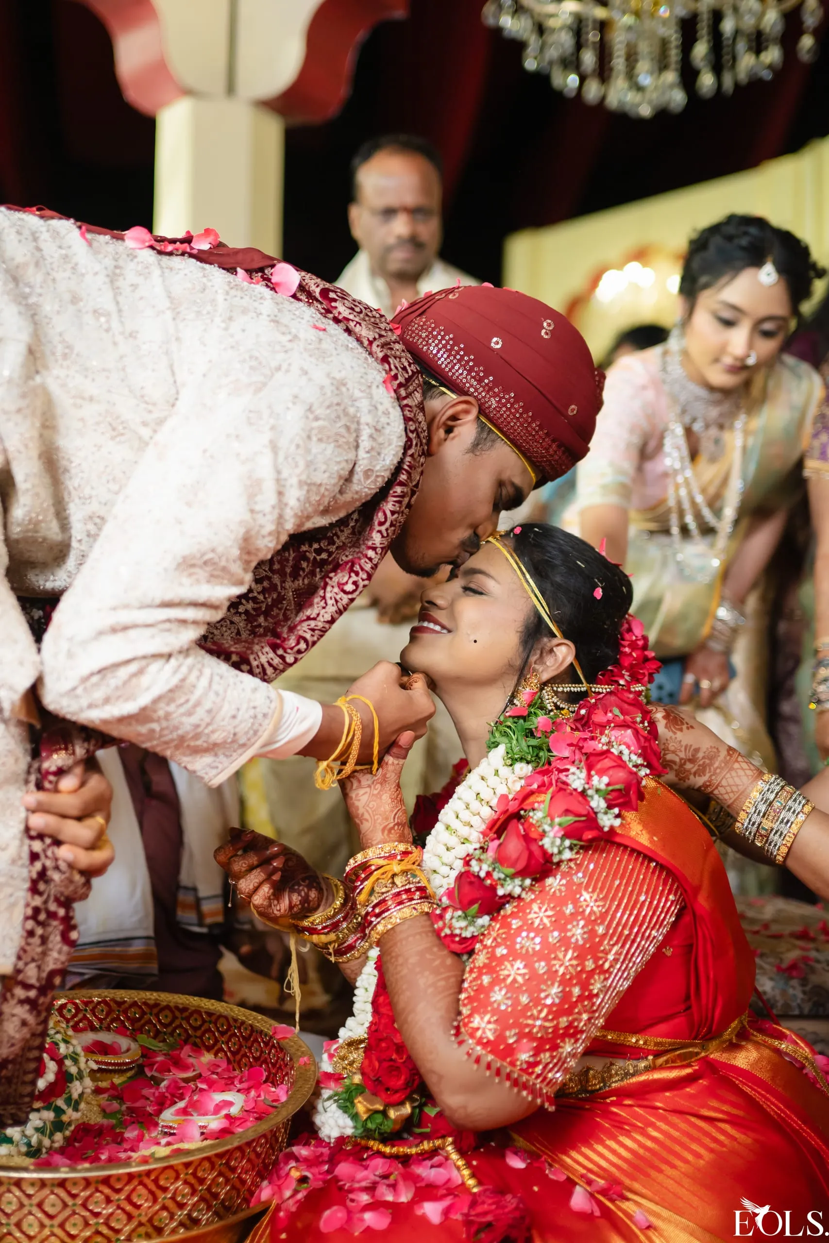 A groom kisses the bride’s forehead, holding her chin.